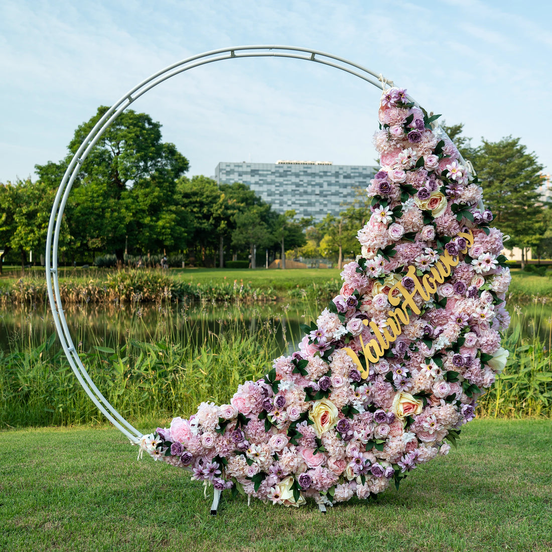 This is a half-covered artificial flower arrangement for a round hoop backdrop, ideal for events or weddings. The design features an asymmetrical cascade of lush pink and purple blooms, punctuated with cream roses and greenery, creating an organic, romantic feel.