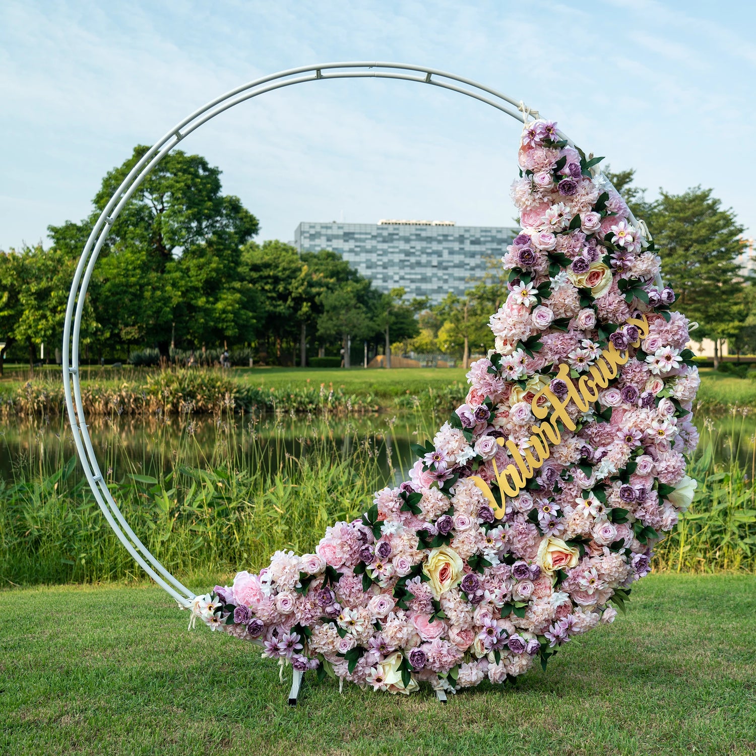 This is a half-covered artificial flower arrangement for a round hoop backdrop, ideal for events or weddings. The design features an asymmetrical cascade of lush pink and purple blooms, punctuated with cream roses and greenery, creating an organic, romantic feel.