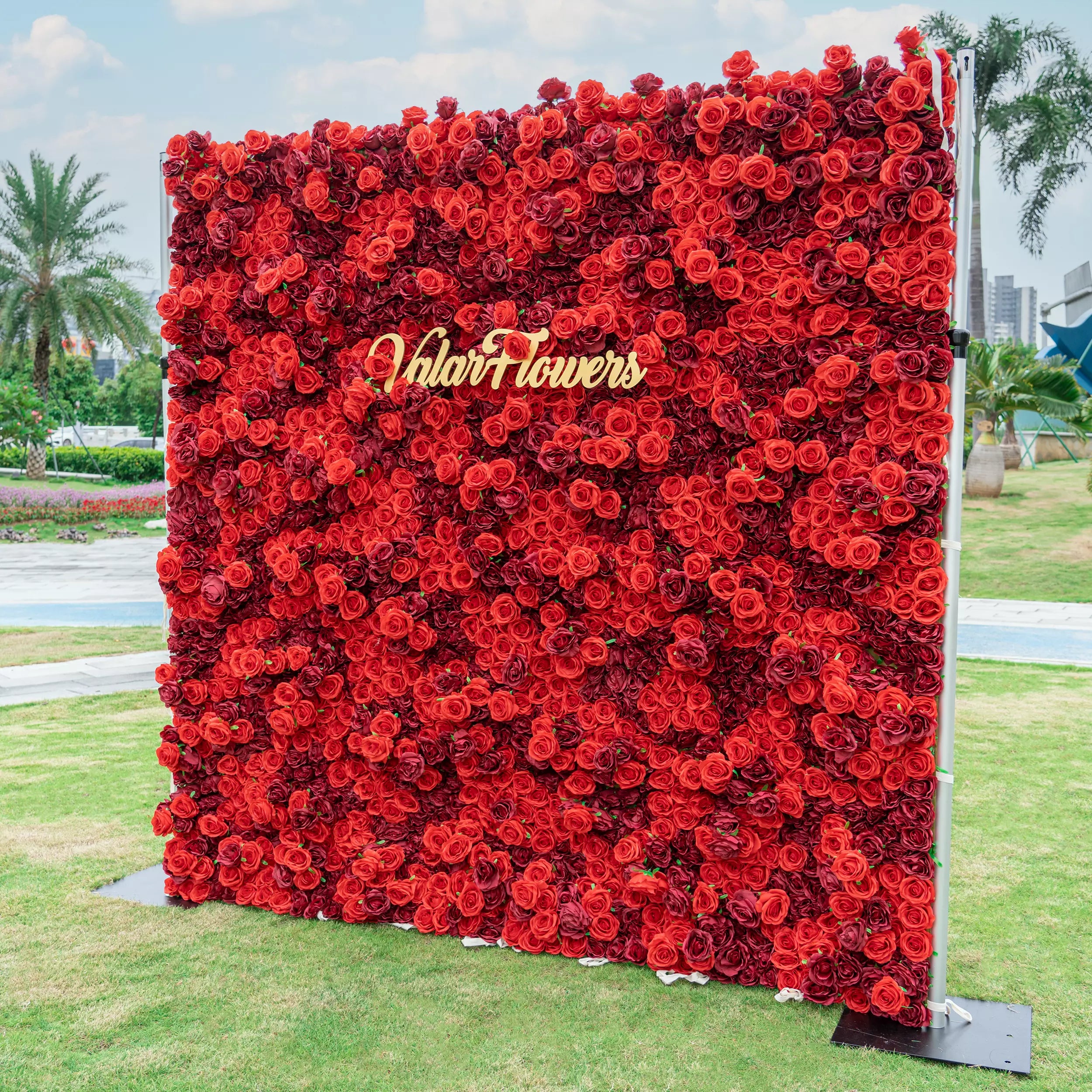 Ruby Rose Radiance: A mesmerizing display of lush, velvety red roses densely packed together, exuding passion and luxury. The golden &quot;VlairFlowers&quot; logo shines brilliantly, nestled among the blooms. Set in an urban park, this opulent floral wall becomes an urban oasis of beauty.