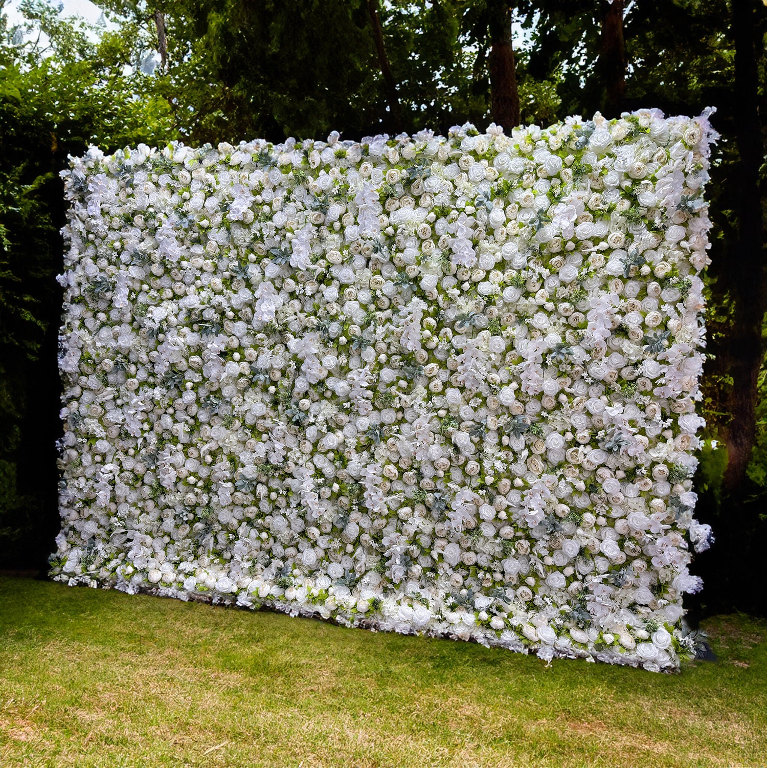 This picture shows a large flower wall, which is predominantly white with a green leafy backdrop. The wall is square - shaped and densely packed with white flowers. It stands on a grassy area, with trees in the background, providing a natural and serene setting. The white flowers appear to be in full bloom, creating a visually appealing and elegant display.