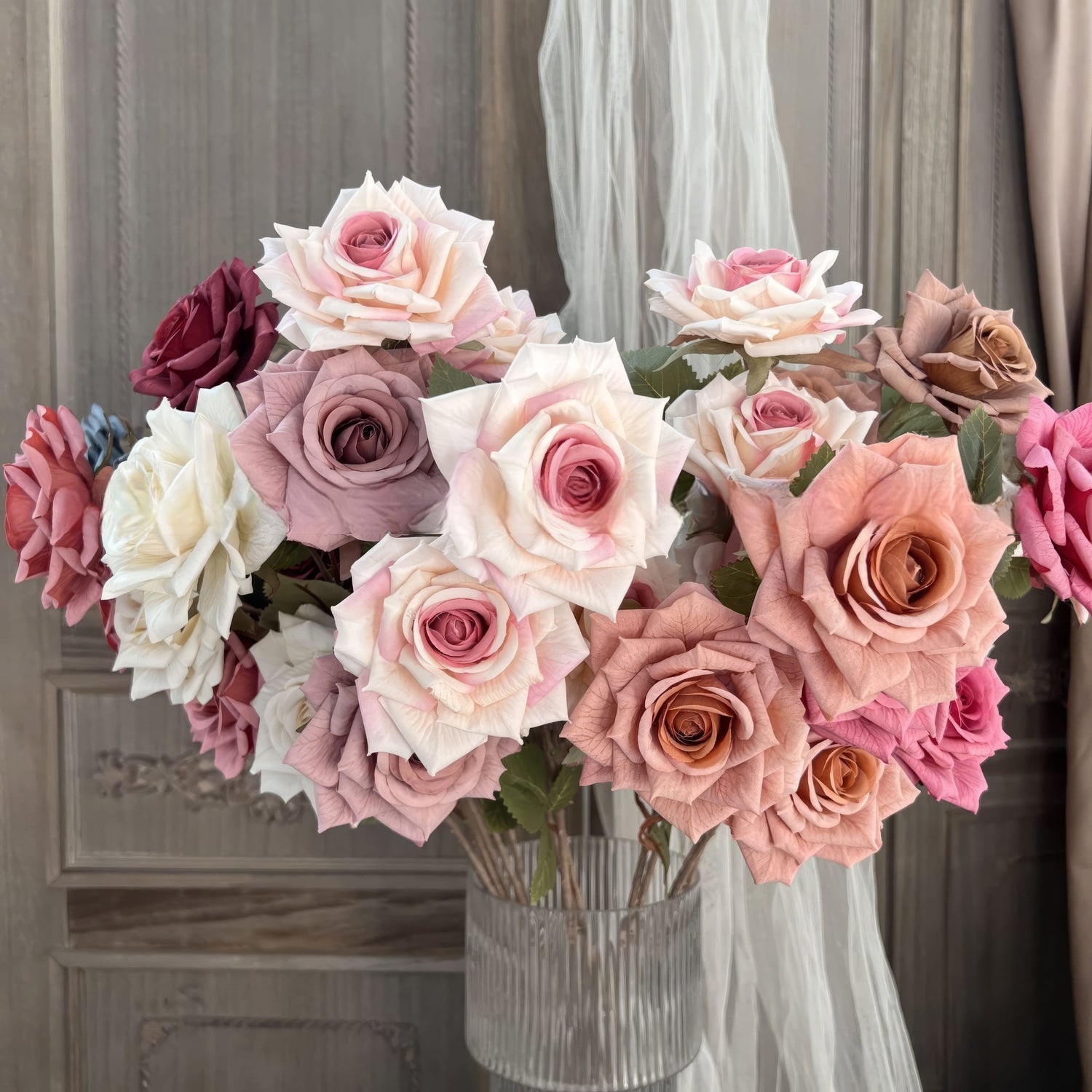 The image showcases a stunning arrangement of roses in various colors, including white, pink, peach, and red, with delicate petals. The bouquet is displayed in a textured glass vase, set against an elegant vintage backdrop.