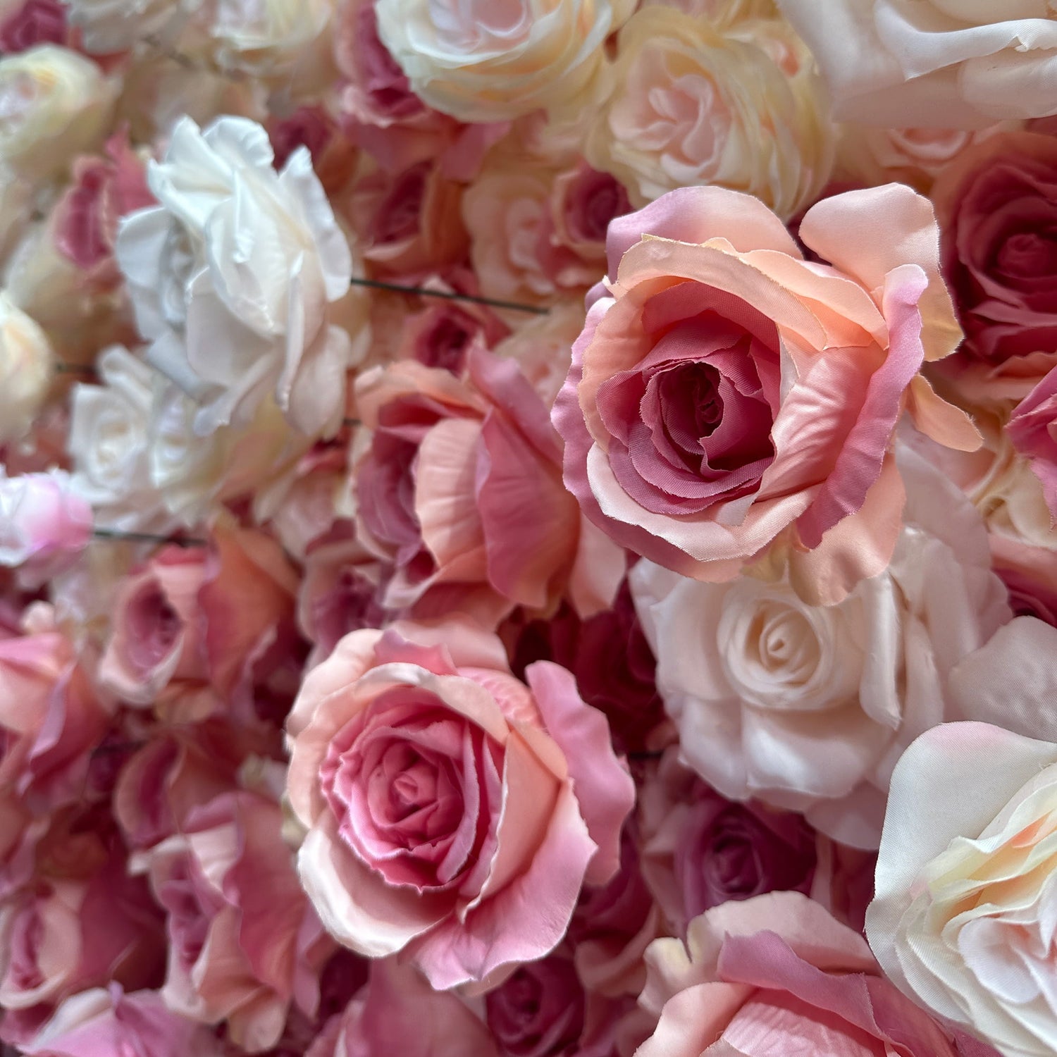 This image showcases a lush arrangement of artificial roses in a harmonious blend of colors. The roses display a range of hues from soft whites and creams to delicate pinks and peaches. The petals are intricately detailed, giving the flowers a realistic appearance. The overall style is romantic and elegant, making it ideal for decorative purposes in events such as weddings or parties. 