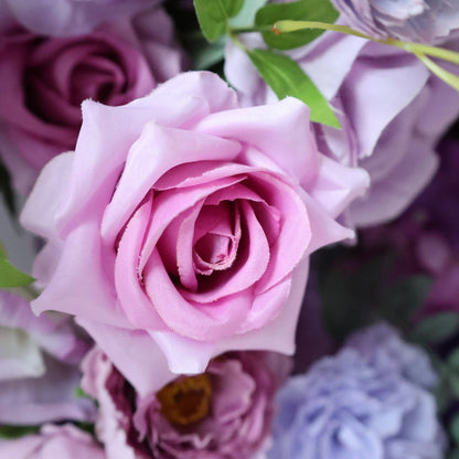 The ValarFlowers arrangement features a prominent light pink rose with soft, ruffled petals. Surrounding it are various shades of purple and pink flowers, creating a romantic and elegant display.