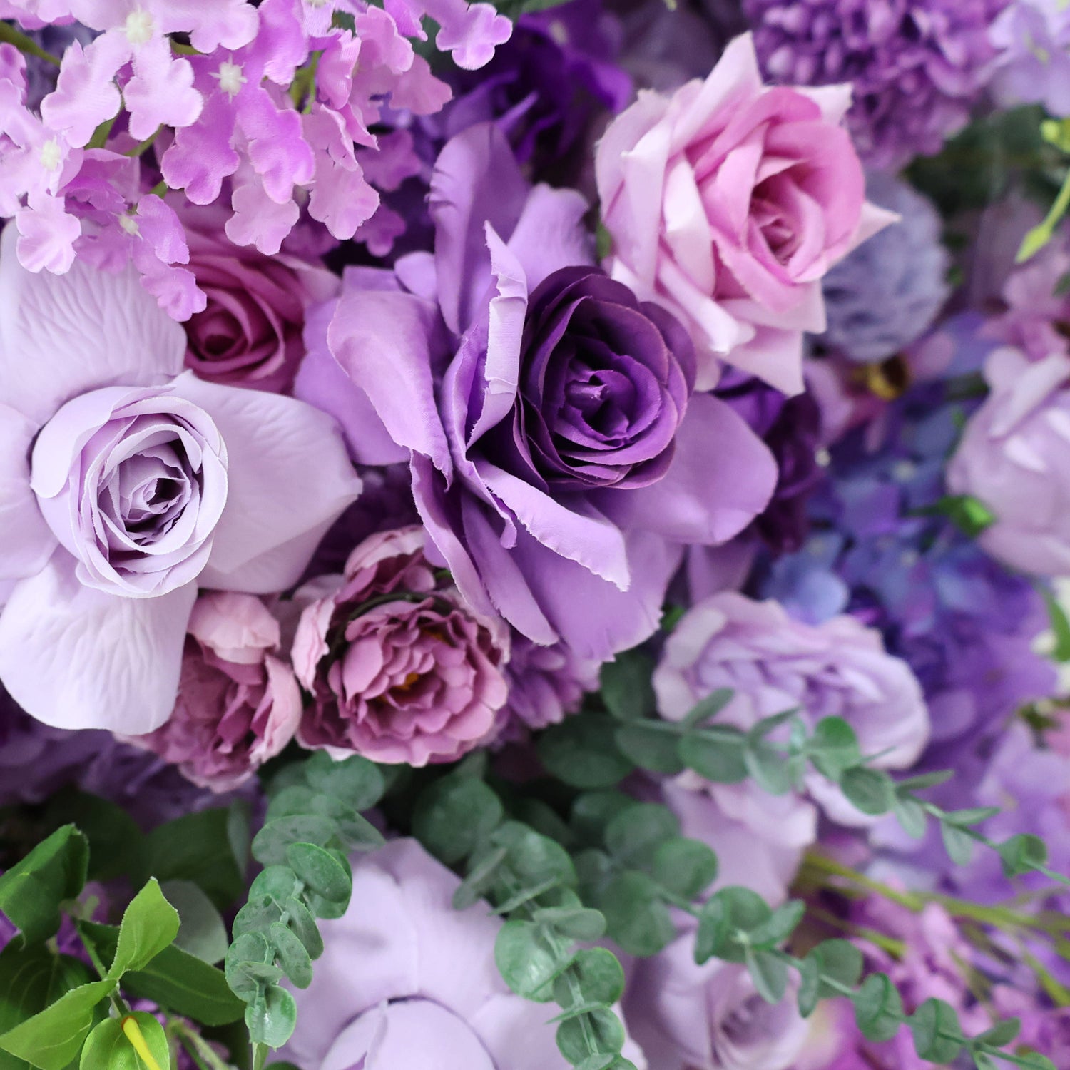 The ValarFlowers bouquet showcases a variety of blooms. It includes light purple roses, soft pink peonies, and clusters of small purple flowers, creating a romantic and elegant arrangement.