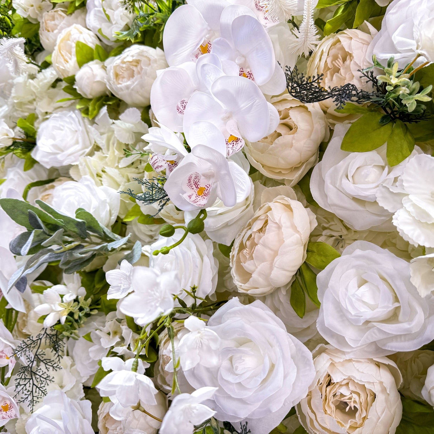 This close - up image focuses on the intricate details of the flower wall. It features a variety of white flowers, including orchids with visible red spots on their petals. The flowers are complemented by green leaves and other foliage, creating a lush and vibrant appearance. The close - up view allows for the appreciation of the delicate textures and natural - looking arrangements of the flowers.