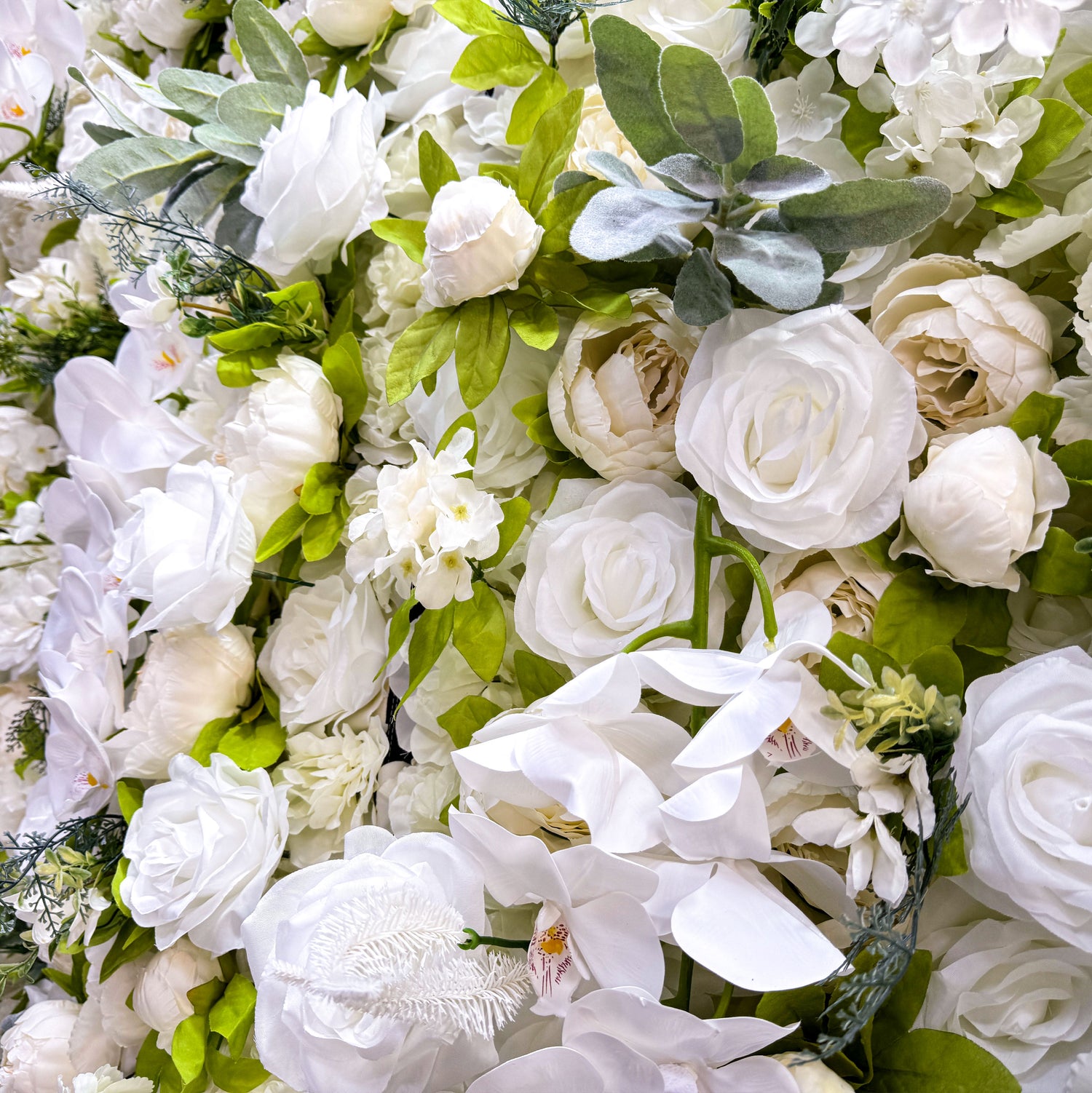 This close - up image focuses on the intricate details of the flower wall. It features a variety of white flowers, including orchids with visible red spots on their petals. The flowers are complemented by green leaves and other foliage, creating a lush and vibrant appearance. The close - up view allows for the appreciation of the delicate textures and natural - looking arrangements of the flowers.