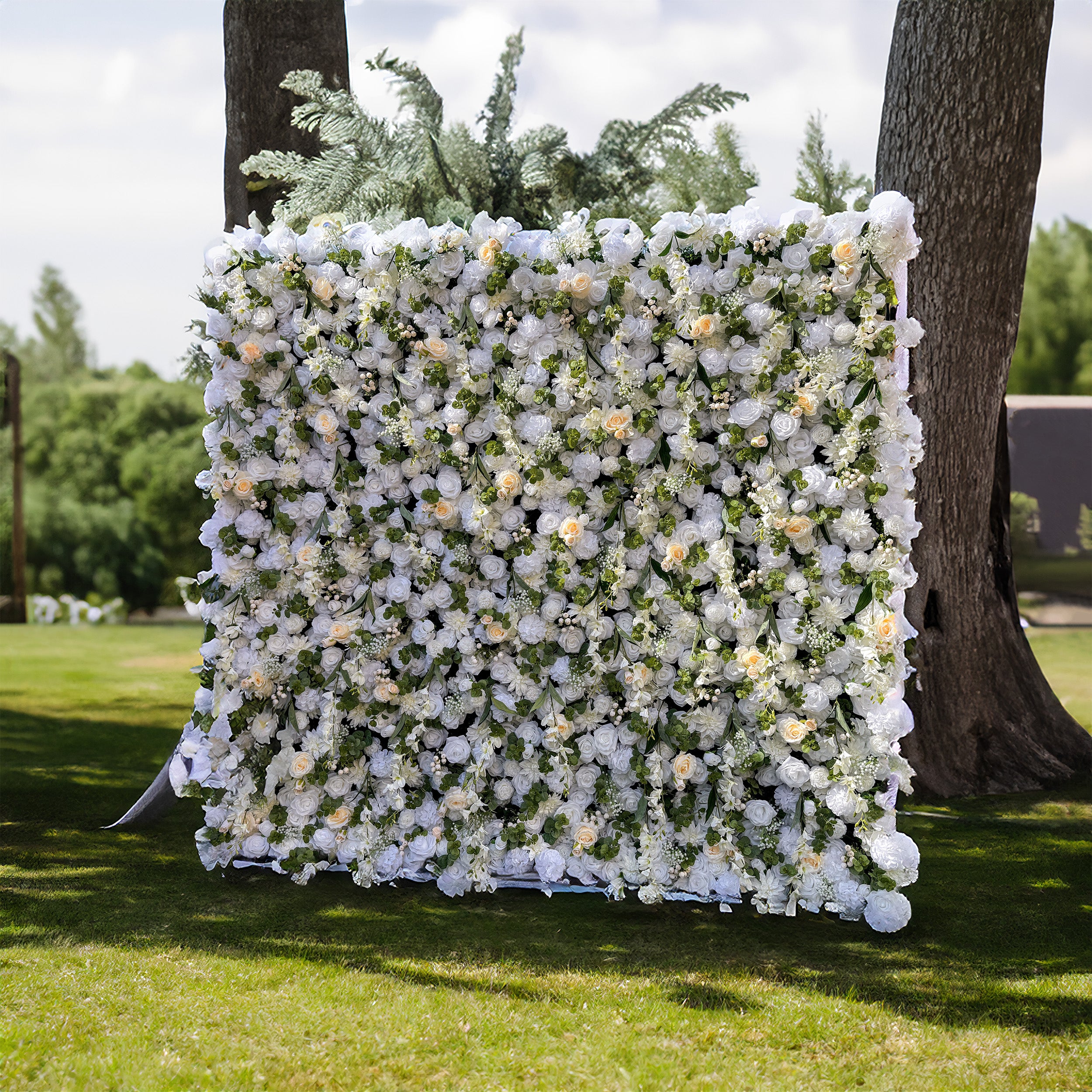 This wedding flower wall is a stunning decoration. It features a dense arrangement of white flowers with some soft - colored blooms interspersed, creating a harmonious and elegant look. The flowers are complemented by lush green foliage. Set against a natural outdoor backdrop, it provides a romantic and picturesque setting for weddings.