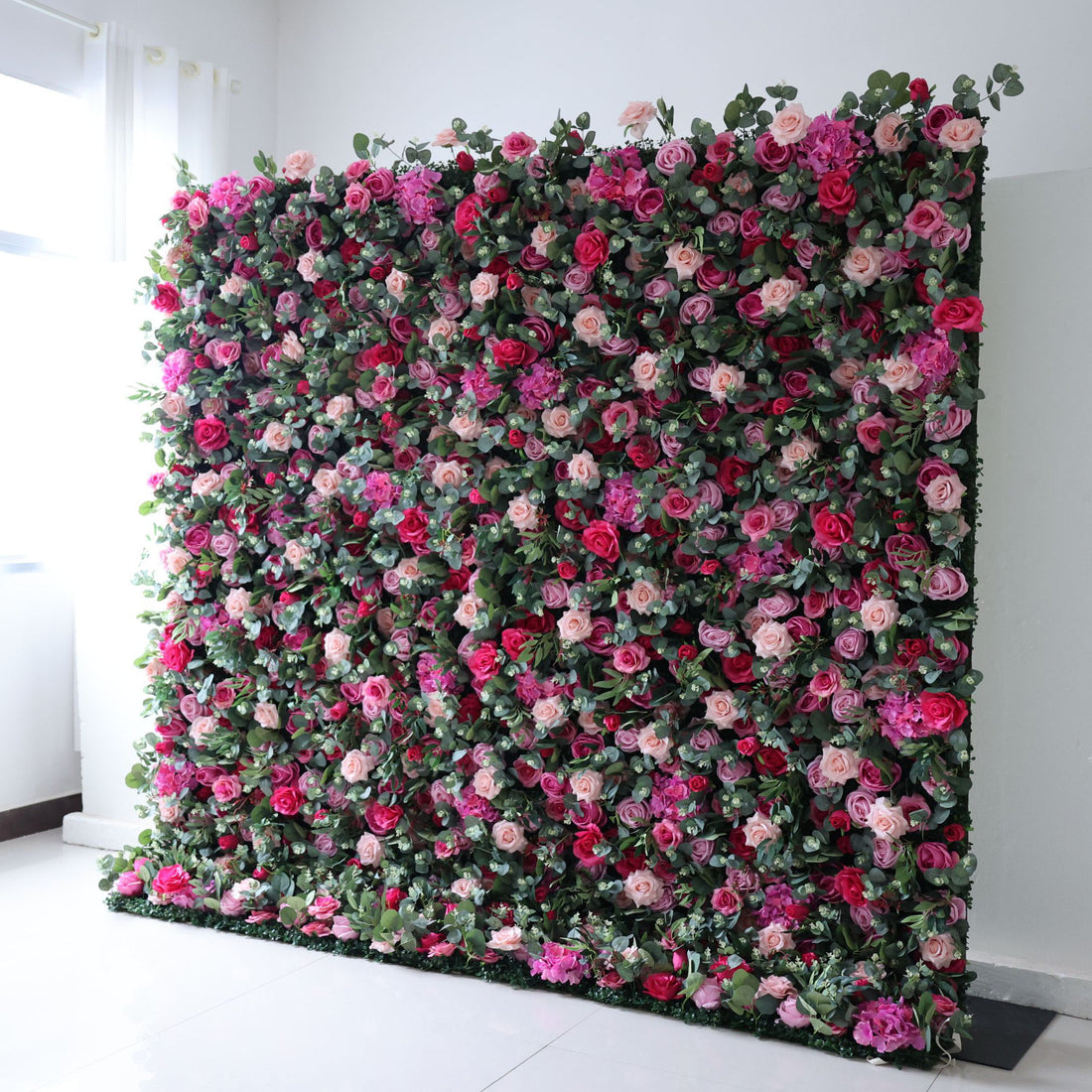 The arrangement features a beautiful combination of pink and white flowers. The flowers are meticulously arranged in an organized manner, creating an eye-catching display. The wall is adorned with various types of flowers, including roses, lilies, and other blooms, strategically placed to create a visually appealing design. 