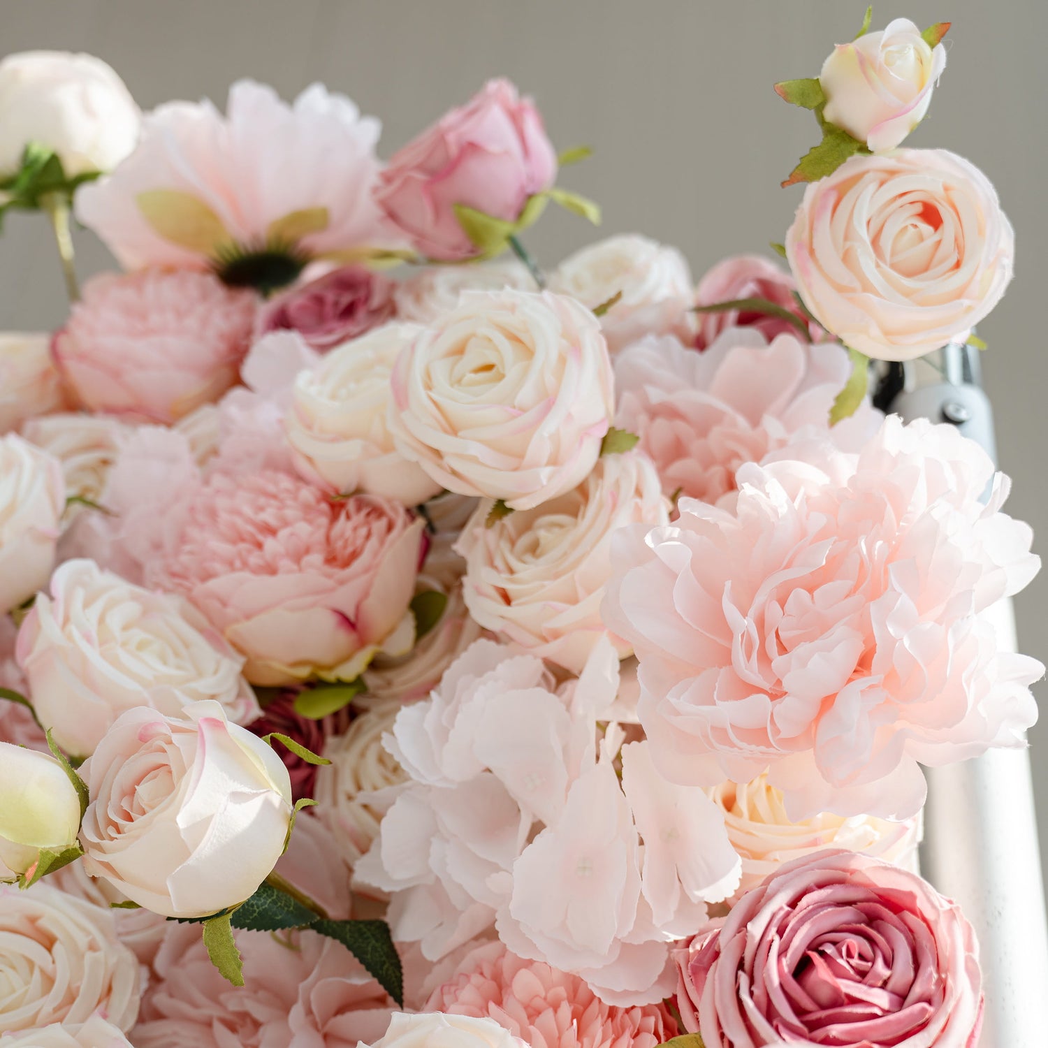 A close - up of a lush arrangement of artificial flowers. The collection features various shades of pink and white roses and peonies, creating a soft and romantic floral display.