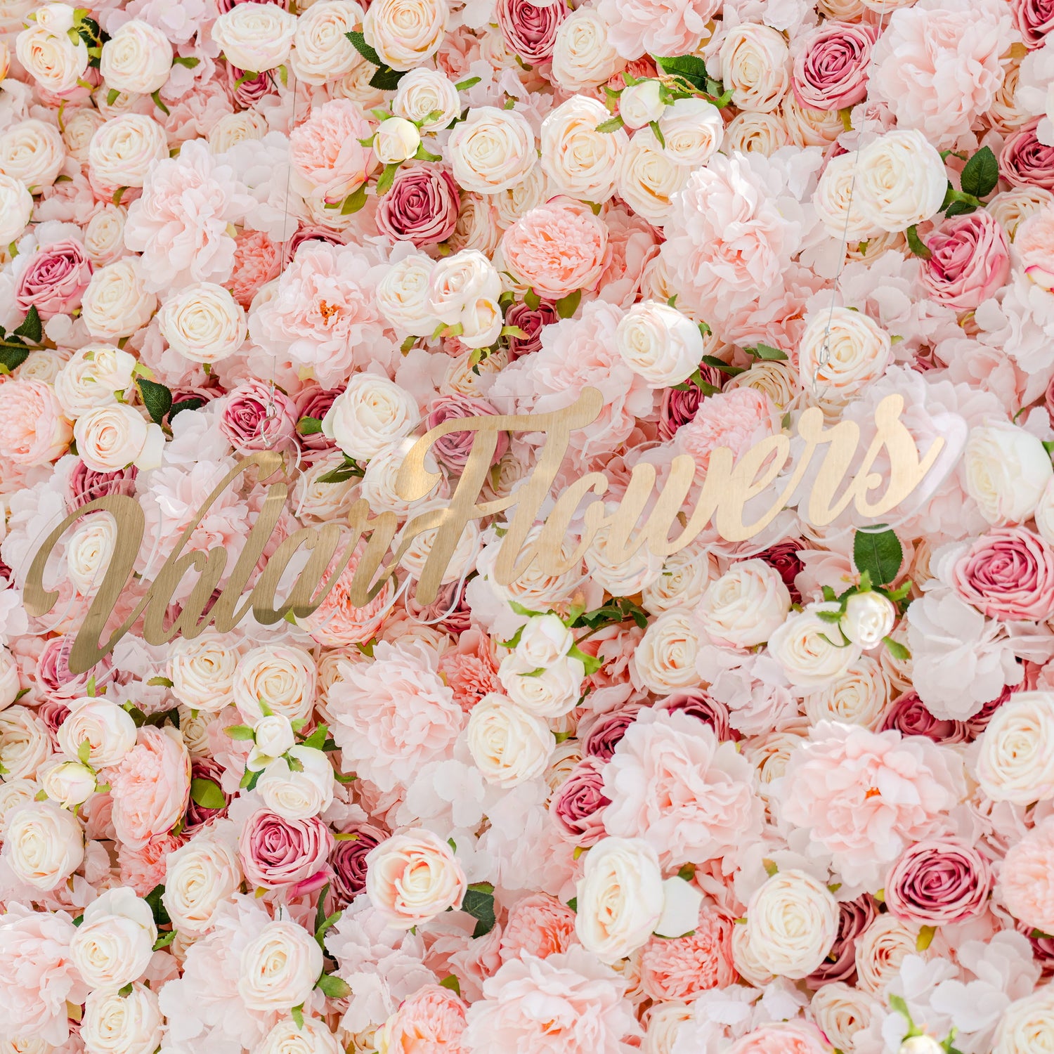 The image features a wall adorned with artificial flowers. The petals have realistic textures and colors, ranging from soft pink to white. The text &quot;ValarFlowers&quot; is prominently displayed, emphasizing the floral theme.