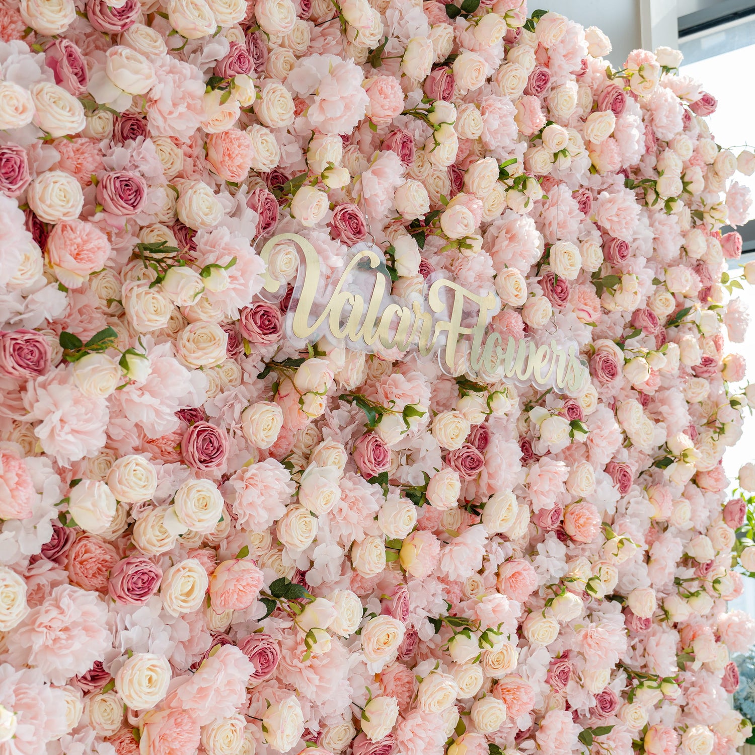 A beautiful flower wall composed of various pink and white roses and peonies. The words &quot;Valar Flowers&quot; are prominently displayed in the center, creating a romantic and elegant atmosphere.