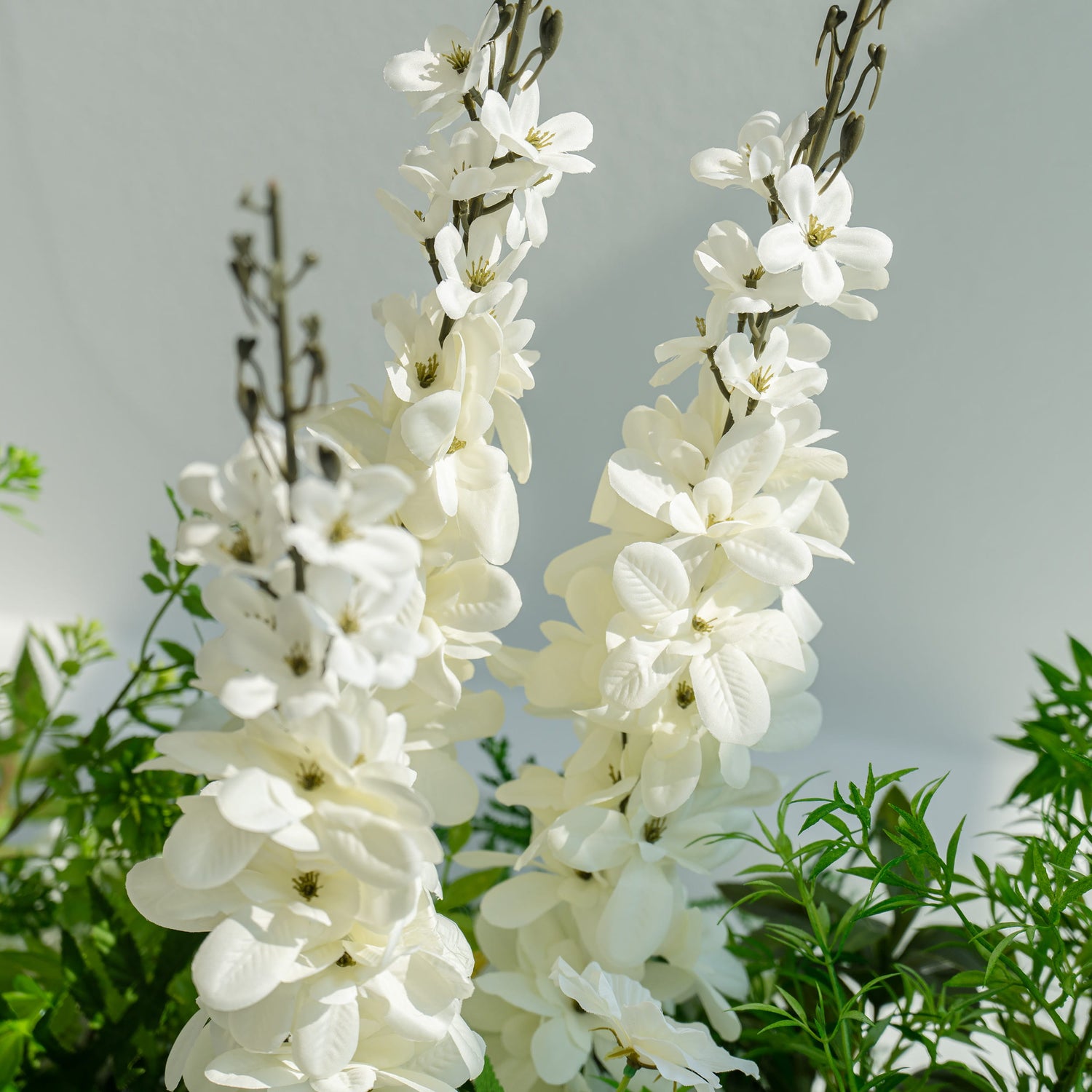 The floral arrangement features tall, elegant white magnolia branches. These branches are surrounded by lush green foliage, creating a fresh and natural look. Ideal for wedding decorations, they add a touch of sophistication and purity to the setting.