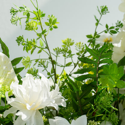 The floral arrangement features a variety of white flowers, including peonies and lilies, surrounded by lush green foliage. This elegant composition is ideal for weddings, creating a romantic and sophisticated atmosphere.