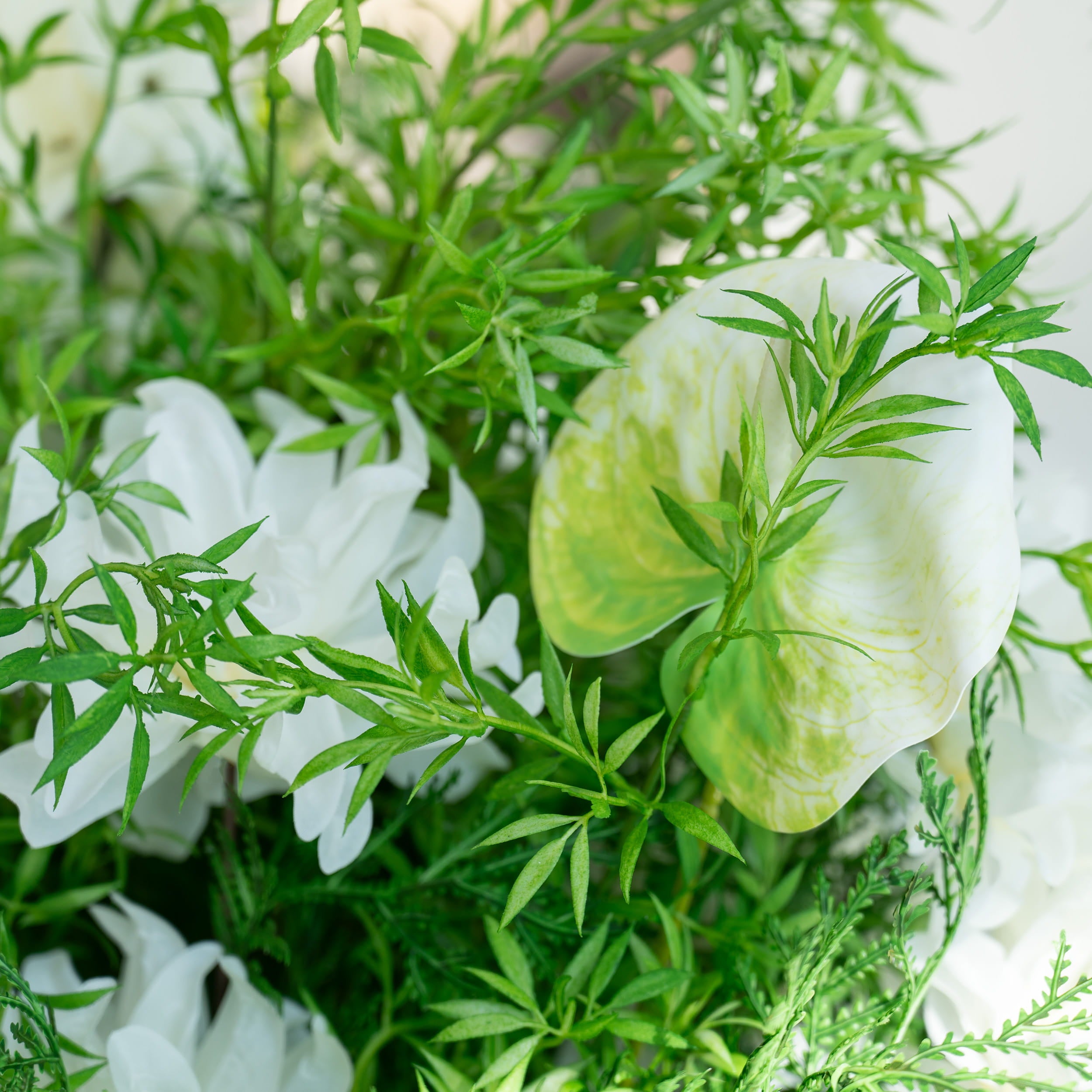 The floral arrangement features a variety of white flowers, including peonies and calla lilies, surrounded by lush green foliage. This elegant composition is ideal for weddings, creating a romantic and sophisticated atmosphere.