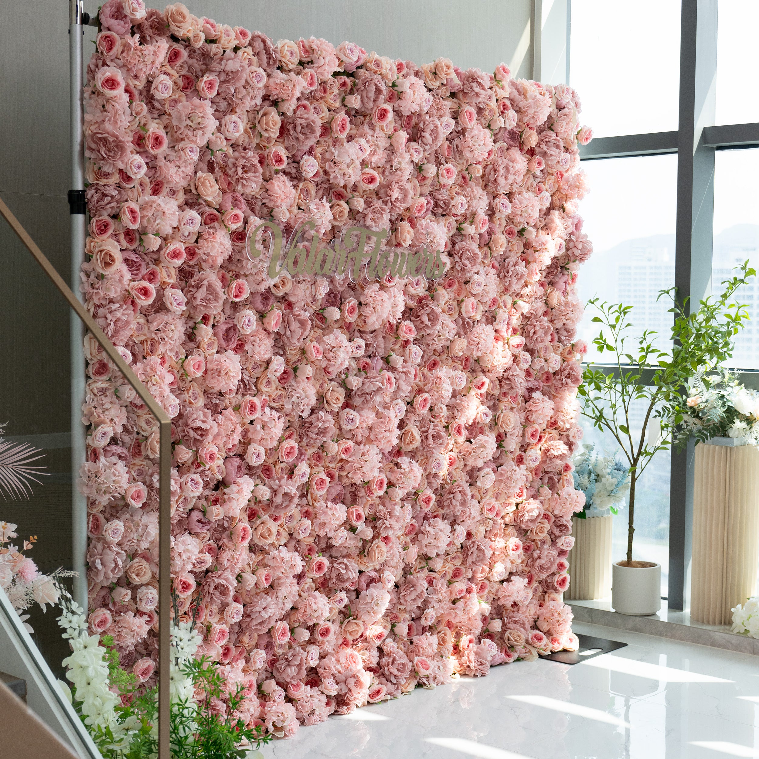 This image features a stunning floral wall adorned with a dense arrangement of light pink and peach - colored flowers. The wall is part of a display that includes the brand name &quot;ValarFlowers&quot; prominently displayed in the center. The overall ambiance is soft, romantic, and inviting, making it ideal for events such as weddings, bridal showers, or romantic celebrations.