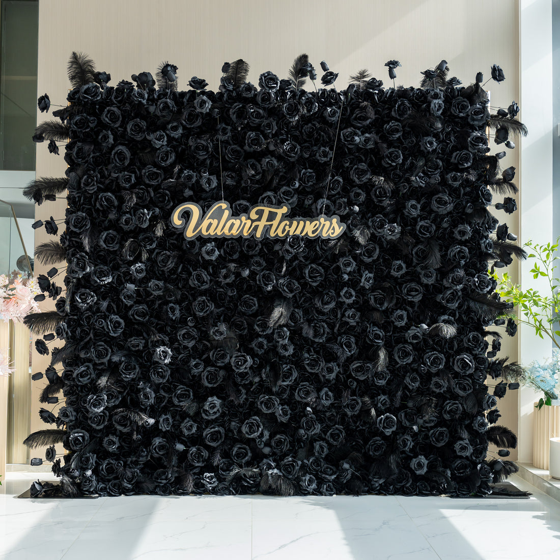 The image features a striking black floral wall with the name &quot;ValarFlowers&quot; prominently displayed in the center. The wall is adorned with black roses and feathers, creating a dramatic and elegant look.
