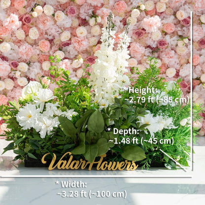 The floral arrangement features a variety of flowers, including white lilies, hydrangeas, and orchids, complemented by lush green foliage. It is ideal for weddings, creating a romantic and elegant atmosphere. The sign &quot;Valar Flowers&quot; adds a charming touch.