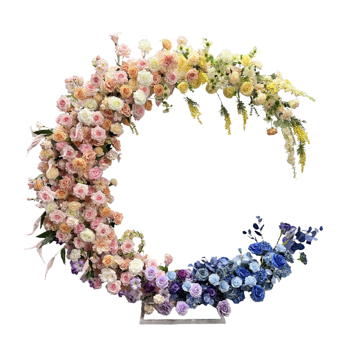 This is a floral arch, intricately designed with a variety of artificial flowers. The arch features a gradient of colors, starting with soft pinks and peaches, transitioning to purples, and ending with blues. The flowers are densely arranged, creating a lush and romantic appearance. This type of arch is commonly used for weddings, photo backdrops, and other celebratory events to add a touch of elegance and charm.