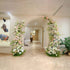 Elegant floral arches with pink and white roses and greenery frame an archway in a sophisticated hallway. The neutral tones and modern decor create a serene and inviting atmosphere, perfect for a chic event or celebration.