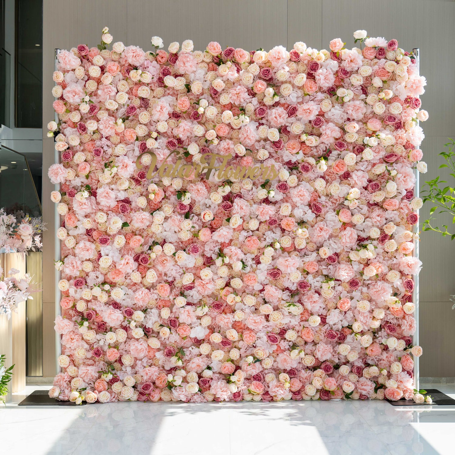 A beautiful flower wall adorned with a variety of pink and cream - colored roses and peonies, featuring the text &quot;Valar Flowers&quot; in the center.